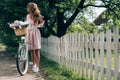 young woman in dress with retro bicycle with wicker basket full of flowers