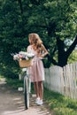 young woman in dress with retro bicycle with wicker basket full of flowers