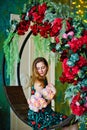 A young woman in a dress sits on a swing with red flowers against a garland of yellow bokeh lights. Holding a bouquet of Royalty Free Stock Photo