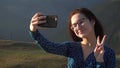 A young woman in a dress stands in the mountains and takes a selfie on a smartphone. The girl travels in the Caucasian Royalty Free Stock Photo