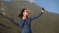 A young woman in a dress stands in the mountains and takes a selfie on a smartphone. Royalty Free Stock Photo