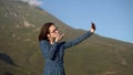 A young woman in a dress stands in the mountains and takes a selfie on a smartphone. Royalty Free Stock Photo