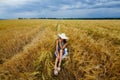 A young woman in a dress and a wide hat, who is sitting in a wheat field before a thunderstorm. Rural landscape in summer Royalty Free Stock Photo