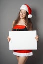 Young woman dressed in christmas costume and santa hat presenting blank sign with copy space