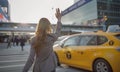 Young woman dressed elegant Business Suit outfit calling yellow taxi cab raising arm gesture in city airport arrival zone.