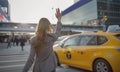 Young woman dressed elegant Business Suit outfit calling yellow taxi cab raising arm gesture in city airport arrival zone.