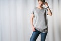 Young woman,dressed in gray t-shirt and blue jeans, standing on light gray background with his hand in pocket of jeans. Royalty Free Stock Photo