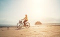 Young woman dressed light summer clothes riding old vintage bicycle with front basket on the lonely low tide ocean white sand Royalty Free Stock Photo