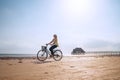 Young woman dressed light summer clothes riding old vintage bicycle with front basket on the lonely low tide ocean white sand Royalty Free Stock Photo