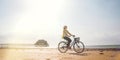 Young woman dressed light summer clothes riding old vintage bicycle with front basket on the lonely low tide ocean white sand Royalty Free Stock Photo