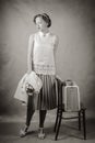 Young woman, dressed in retro style, with a jacket in her hands and a suitcase on a chair Royalty Free Stock Photo