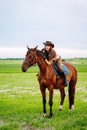 Young woman dressed in riding clothes and hat riding brown horse in green field Royalty Free Stock Photo