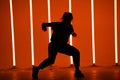 Young woman dressed in street fashion wear dancing hip-hop style in a studio with neon lighting tube on a orange Royalty Free Stock Photo
