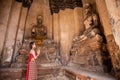 Young woman dressed in traditional red Thai dress and golden ornaments stands Worship Buddha statues greeting in the ancient site