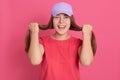 Young woman dresses red t shirt and baseball cap posing isolated over pink background, holding her hair in hands like wants make