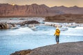 Young woman dressing yellow cold clothes seeing the amazing Jokulsarlon, iceberg lagoon in Iceland, mountains in the background