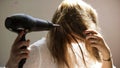 A young woman dries her hair with a hairdryer  on a beige wall background. Art. Young blond woman in a white Royalty Free Stock Photo