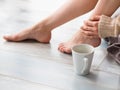 Young woman drinking cappuccino coffee and sitting on the wooden floor. Close up of female legs and cup of coffee Royalty Free Stock Photo