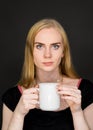 Young woman drinking coffee. Blonde girl with white tea cup on a gray background. Royalty Free Stock Photo