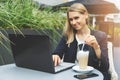 Young woman drinking coffee latte at cafe outdoor terrace and working with laptop. freelance remote work Royalty Free Stock Photo