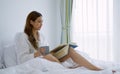Young woman drinking coffee while reading a book sitting on the bed in the morning Royalty Free Stock Photo