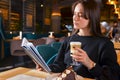 Young woman drinking coffee and reading book sitting indoor in urban cafe or restaurant Royalty Free Stock Photo