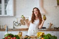 Young woman drinking green smoothie and fresh water with cucumber, lemon, leaves of mint on the kitchen table with fruits and Royalty Free Stock Photo