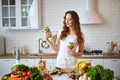 Young woman drinking green smoothie and fresh water with cucumber, lemon, leaves of mint on the kitchen table with fruits and Royalty Free Stock Photo