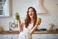 Young woman drinking green smoothie and fresh water with cucumber, lemon, leaves of mint on the kitchen table with fruits and Royalty Free Stock Photo