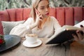 Young woman drinking hot coffee and talking on phone in sidewalk cafe while holding notebook Royalty Free Stock Photo