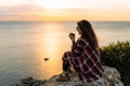 Young woman drinking tea from her thermos, enjoying autumn evening by the sea. A woman meets the sunset on the sea. Royalty Free Stock Photo