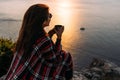 Young woman drinking tea from her thermos, enjoying autumn evening by the sea. A woman meets the sunset on the sea. Royalty Free Stock Photo