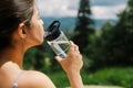 Young woman drinking water from bottle after training at sunny mountain hills. Outdoor workout