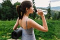 Young woman drinking water after training at sunny mountain hill. Outdoor workout. Healthy lifestyle Royalty Free Stock Photo