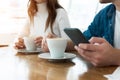 Young woman drinks coffee with her husband, he holds smarthone and texts message, multitasking concept Royalty Free Stock Photo