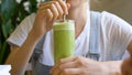 Young woman drinks green fresh beverage in vegetarian cafe