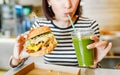 Woman drinks green smoothies and eats a burger in a vegan fast food restaurant