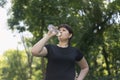 Young woman drinks water from the bottle after jogging in the spring park. Drinking regime during sports. Body positivity Royalty Free Stock Photo