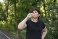 Young woman drinks water from the bottle after jogging in the spring park. Drinking regime during sports. Body positivity Royalty Free Stock Photo