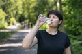 Young woman drinks water while jogging in the park. Drinking regime during sports Royalty Free Stock Photo