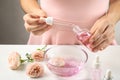 Young woman dripping rose essential oil into glass bottle at table Royalty Free Stock Photo