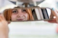 Young woman driver checking rear view mirror looking backwards while driving a car