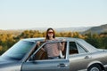 A young woman driver looks out of the car at the autumn landscape and smiles satisfactorily Royalty Free Stock Photo
