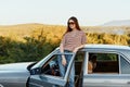 A young woman driver looks out of the car at the autumn landscape and smiles satisfactorily Royalty Free Stock Photo