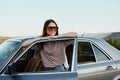 A young woman driver looks out of the car at the autumn landscape and smiles satisfactorily Royalty Free Stock Photo