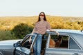 A young woman driver looks out of the car at the autumn landscape and smiles satisfactorily Royalty Free Stock Photo