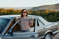 A young woman driver looks out of the car at the autumn landscape and smiles satisfactorily Royalty Free Stock Photo