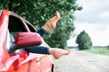 Young woman driver resting in a red car, put her feet on the car window, happy travel concept Royalty Free Stock Photo