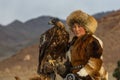 Young woman Eagle Hunter at traditional clothing, while hunting to the hare holding a golden eagles on his arms