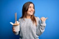 Young woman eating asian noodles from take away box using chopstick over blue background pointing and showing with thumb up to the